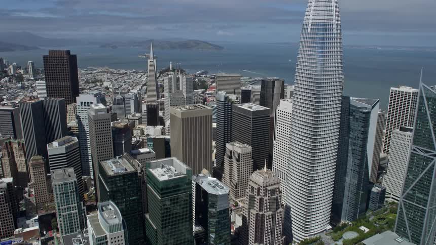 Aerial footage flying over Downtown San Francisco towards North Beach piers on a sunny day showcasing high rise buildings skyscrapers and the iconic landmarks of the city