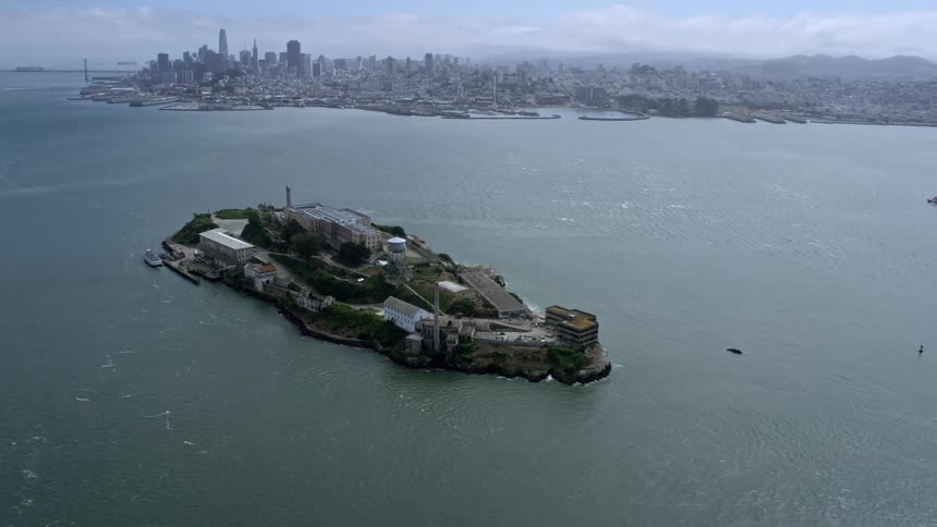 Aerial footage of Alcatraz Island and downtown San Francisco skyline showcasing the cityscape and iconic structures in cloudy skies during daytime in California