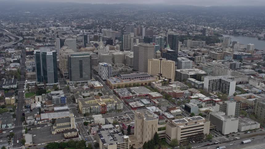  aerial stock footage of traffic running on the freeway beside downtown office buildings in Oakland on a foggy day providing a side view of the city and capturing the industrial atmosphere of Northern California's Bay Area during summer