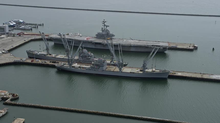  aerial footage showcasing passing an aircraft carrier and Naval ships docked in Alameda California during a cloudy day captured with a Shotover F1 camera providingview of the seafaring vessels and the USS Hornet at the naval air station