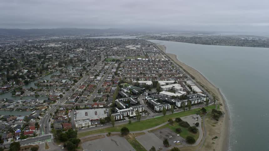  aerial footage showcasing the approaching waterfront neighborhoods of Alameda California capturing the residential district of a coastal city on a cloudy day in the Bay Area during summer