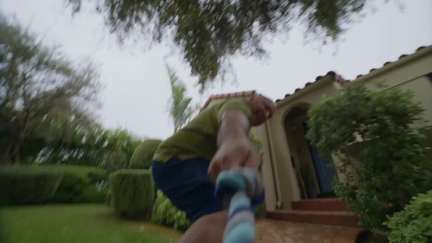 Hispanic man outdoors grabbing and pulling a rope toy from the mouth of a dog outside the frame during day time