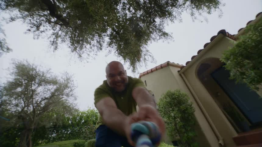 A man pulls on a tug toy in a yard in front of a house