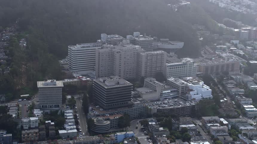 aerial footage capturing the passing view of a hospital in the Inner Sunset District San Francisco California on a partly cloudy day showcasing the medical center and surroundings in the bustling city