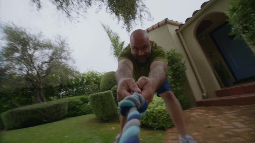 A man is playing tug of war with his dog and a rope