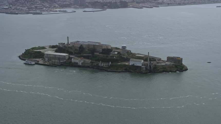 Aerial footage of Alcatraz Island as a ferry passes by in San Francisco Bay showcasing the historic landmark and government building