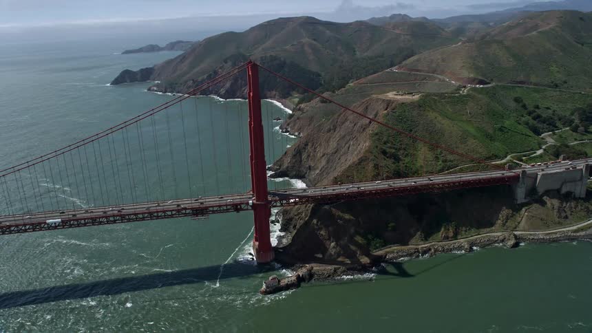  aerial footage of a day time orbit around one of the towers on the iconic Golden Gate Bridge in San Francisco California showcasing the city skyline partly cloudy skies and transportation