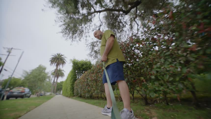 Man walking on the sidewalk holding a leash as if walking a dog outside the frame during day time