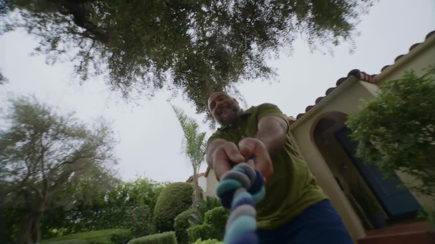 Man pulling a dog toy rope in the backyard