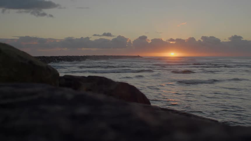 Waves slowly wash upon a rocky coastline as the sun is set low in the sky