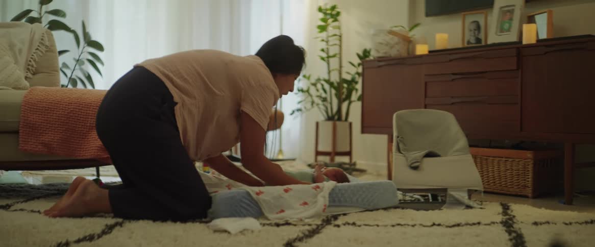 A mother leans over to place her baby on a bed and kisses its forehead