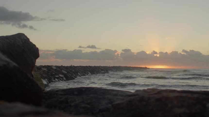 Ocean waves wash upon a rocky shoreline as the sun is set low in the sky