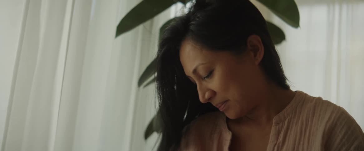 A mother holding her newborn baby nursing them in front of a window letting in daylight