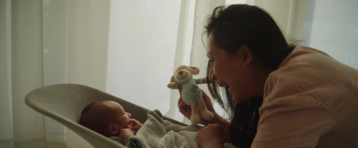 A young mother holds a small stuff toy near her babys head