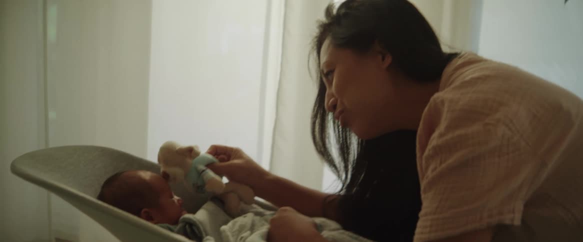 A mother smiles as she holds out a stuffed toy for her newborn baby