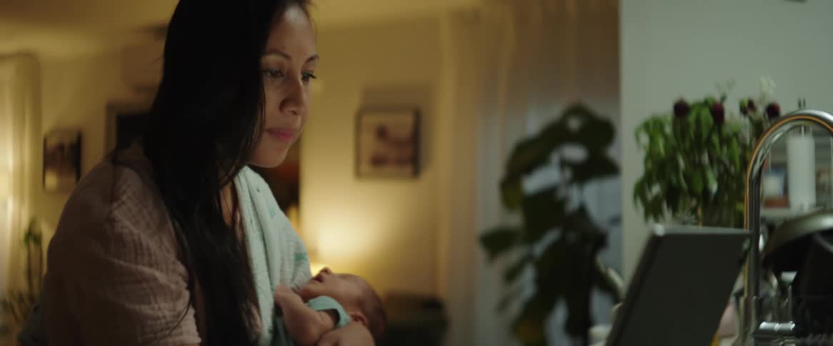 Mother hold her baby while operating a laptop indoor