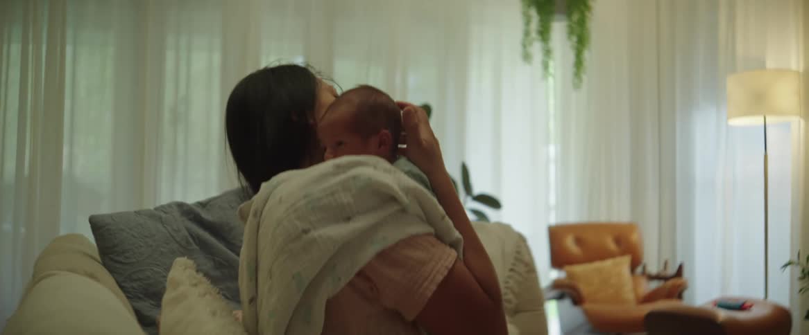 A woman picks up a tiny baby and holds it on her shoulder while patting its back