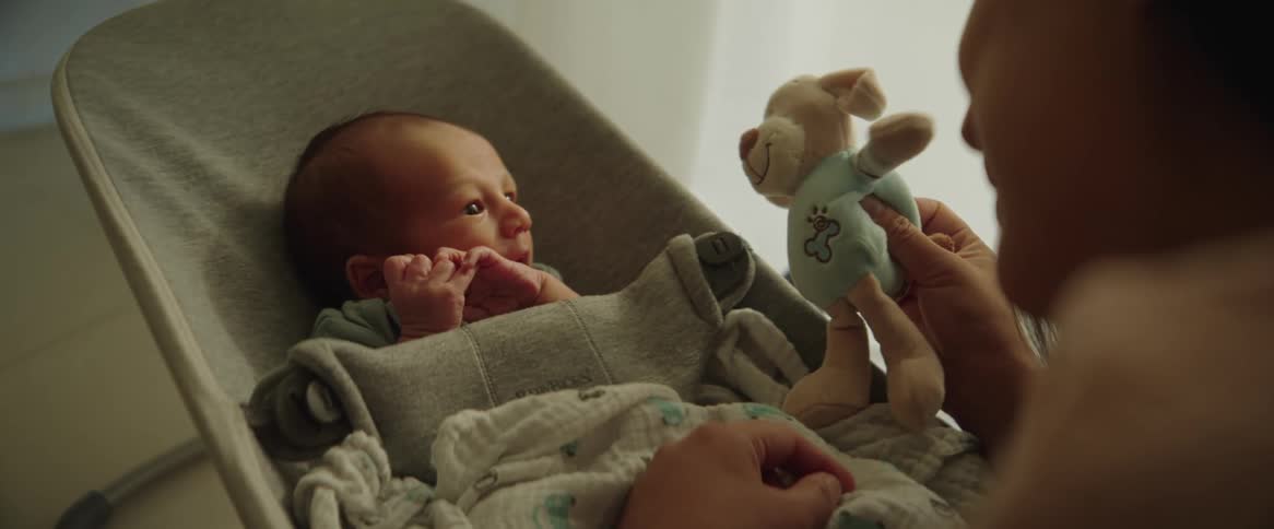 A mother plays with her newborn son with a teddy bear