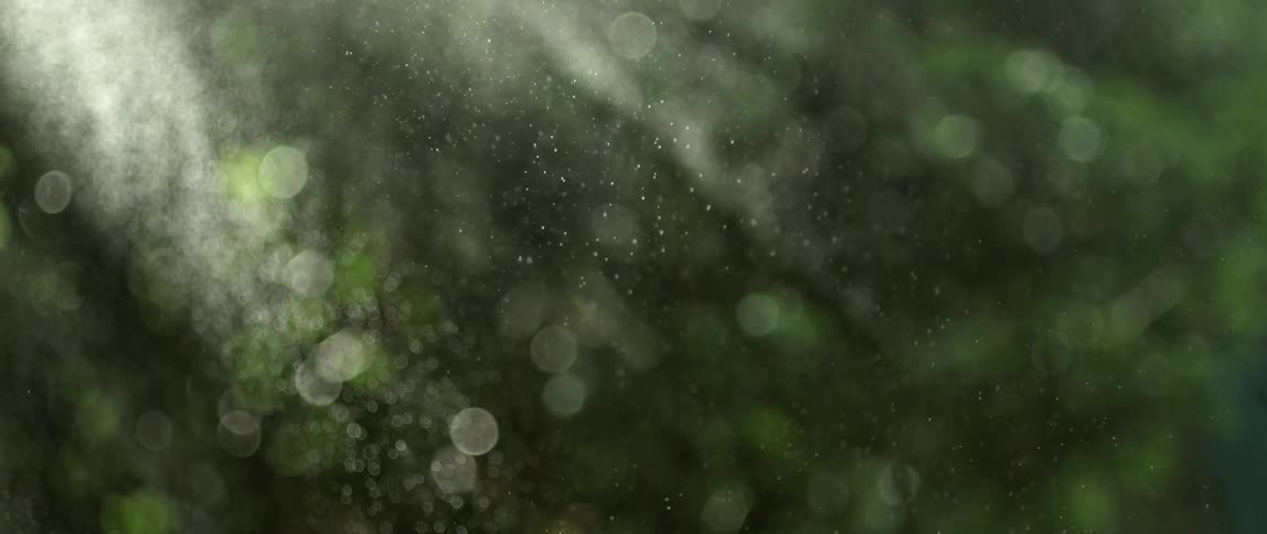 Abstract drops of water slowly falling on a landscape with grass and trees in the sun