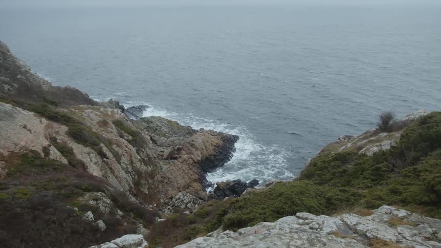 Aerial of a rocky coast as ocean waves crash against the coast during the day