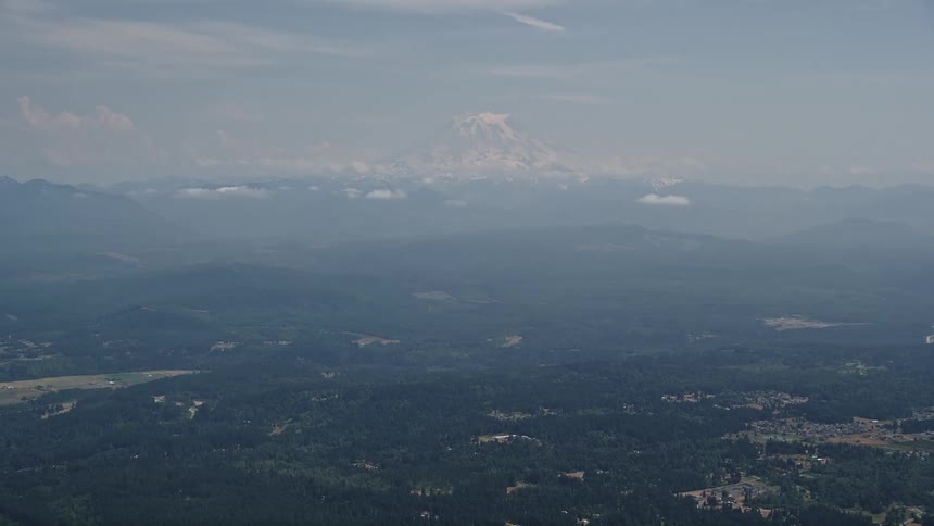 Aerial footage of Mount Rainier an active volcano in Washington's Cascade Range with snowy peaks surrounded by partly cloudy skies and lush green landscapes