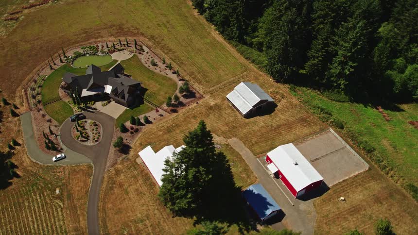 Aerial footage of a large farmhouse with red barns in La Center Washington showcasing a circular driveway leading to the house across a field from the farm buildings