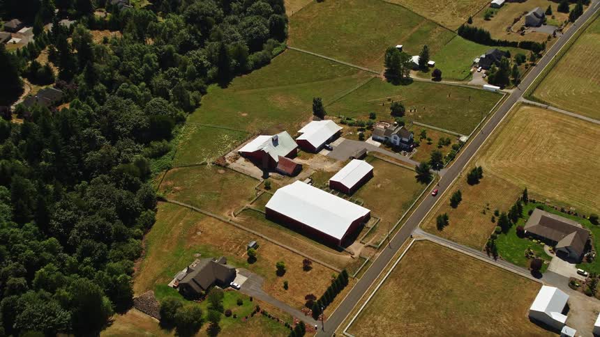 Tilting down from a bird's eye view thisaerial footage captures the idyllic scene of farmhouse and barns nestled beside a country road in La Center Washington during daytime