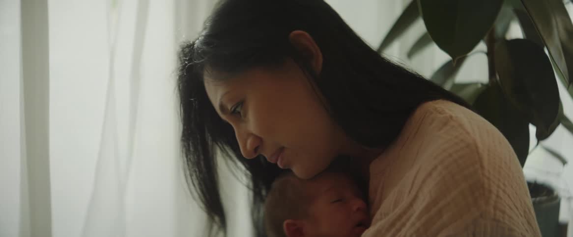 Mother smiles while holding baby against her chest in home