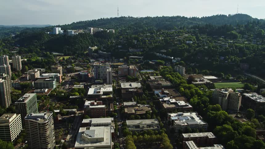 an aerial view of Downtown Portland Oregon as the camera tilts up from the Steel Bridge revealing the vibrant metropolis with towering skyscrapers surrounded by the natural beauty of the Willamette River
