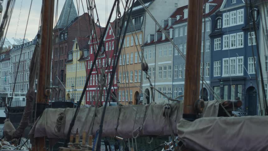 Ship sails and masts in front of colorfully painted buildings built close together during the mid morning