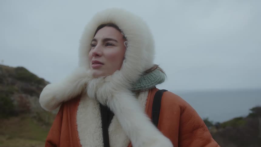 Beautiful woman wearing a white mink hood next to the ocean on a windy day