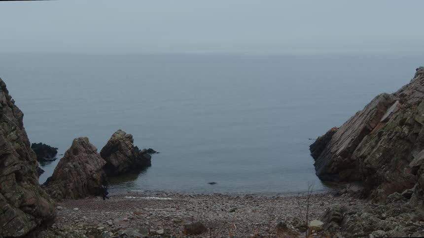 Person walking on the shore of the deserted beach on a cloudy day