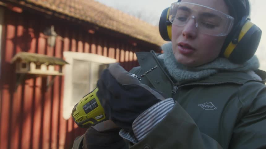 Woman wearing protective gear assembles an electric drill outdoors