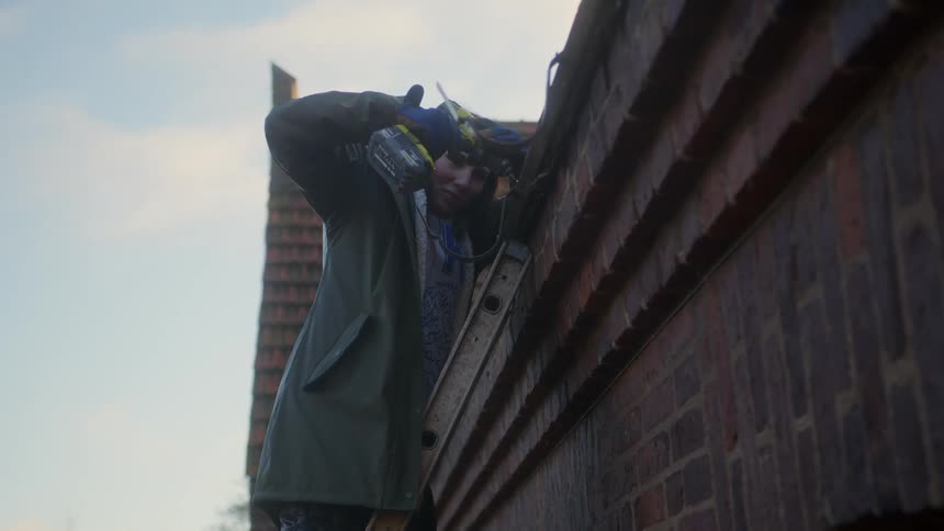 Woman atop a ladder does home repairs on the house exterior
