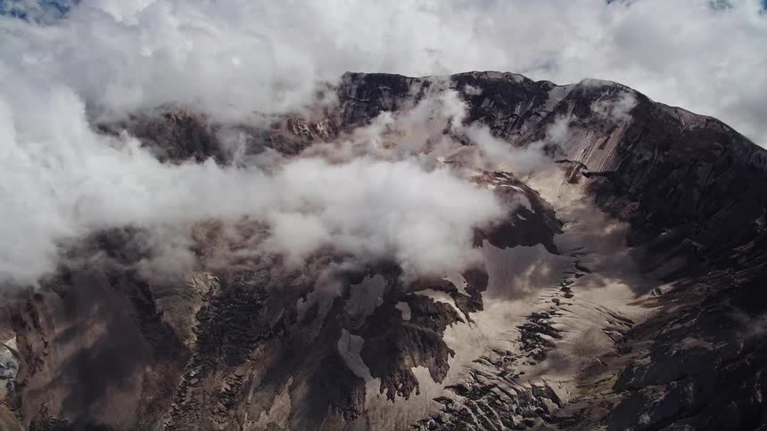 Approaching the Mount St Helens crater this aerial footage captures a mountain peak surrounded by low clouds in Washington