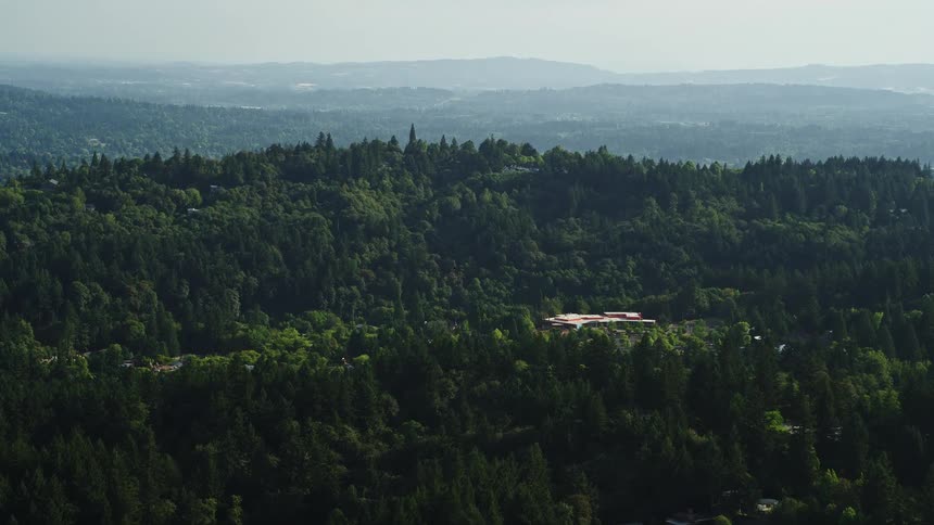 Aerial view of tree-covered hills approaching Portland Children's Museum in Southwest Portland Oregon on a sunny day