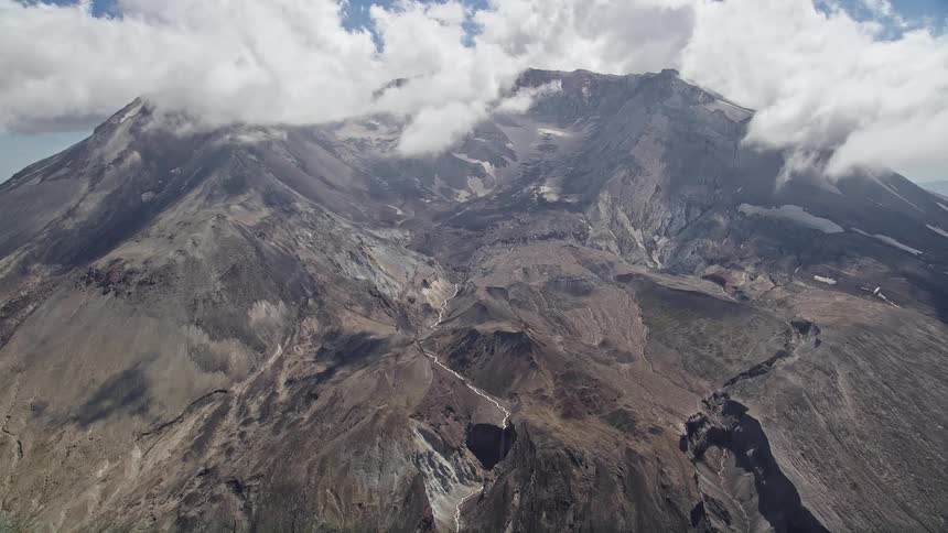 Aerial pass over Mount St Helens crater with clouds during a partly cloudy day in Washington