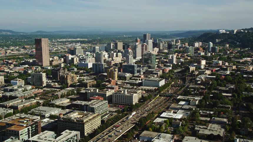High-rise buildings and skyscrapers tower over heavy traffic on Interstate 405 in downtown Portland Oregon during a sunny day