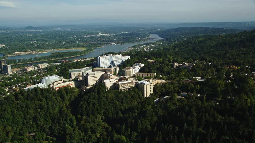 Aerial footage of Oregon Health and Science University and downtown Portland in the distance showcasing the high rise buildings and cityscape surrounded by nature