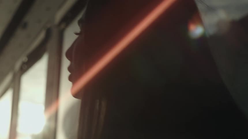 Close up of a woman standing outside with the sun glaring across her face as she sits in front of a building