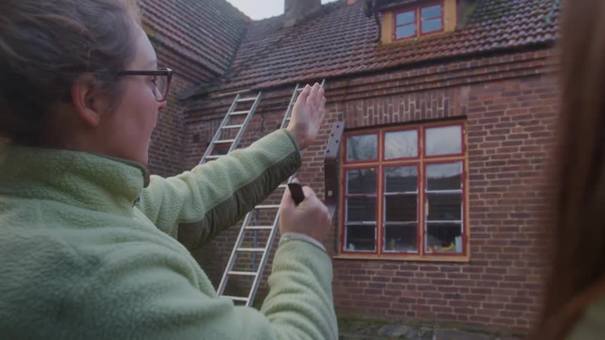 A woman holding an object and pointing to a wall explaining something to someone else