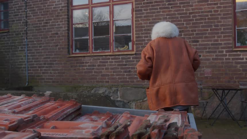 A woman in thick coats picking up a tile that is piled up with others and leaving