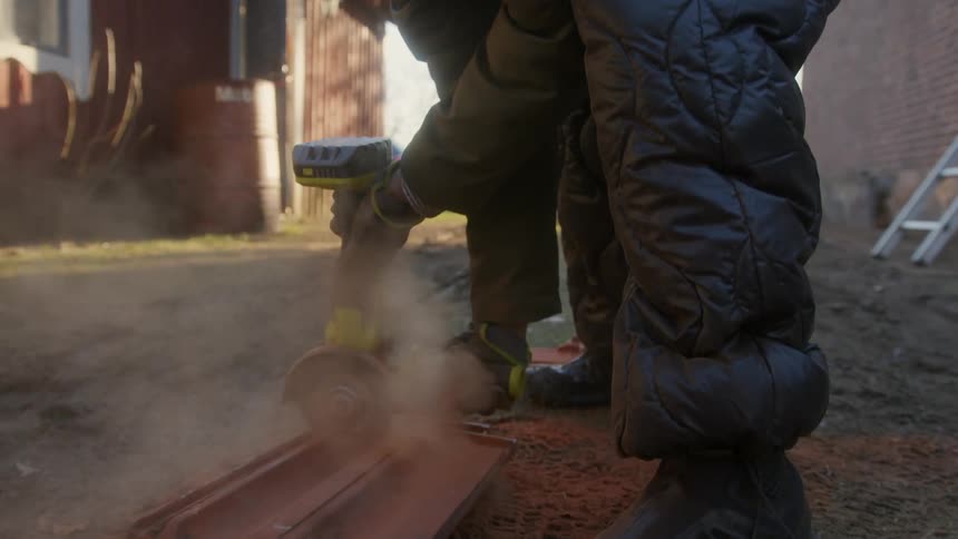Close up of a woman wearing coat pants and hat while she bends over sanding something