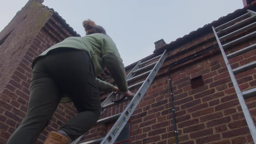 Woman walking up a ladder propped against a brick wall as she stops in the middle