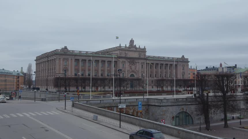 A large architectural building on a cold cloudy day with bare trees in front of it in the middle of a city