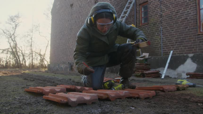 Women working outside in the cold wearing a coat and pants while measuring red bricks on the ground during the day