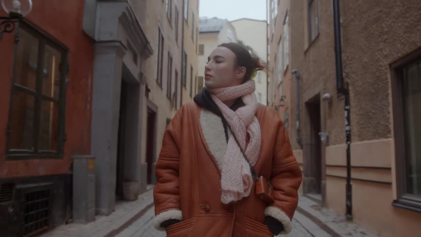 Woman wearing coat and scarf walking and observing architecture of old buildings around