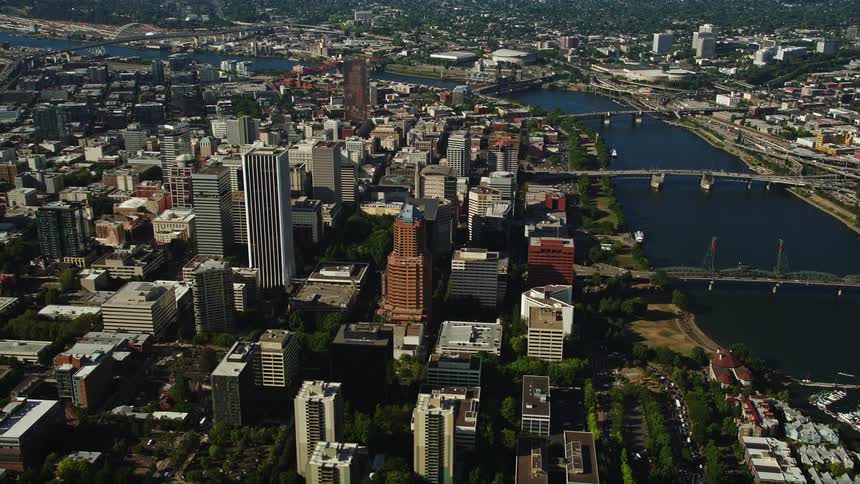 Drone footage capturing the stunning cityscape of downtown Portland Oregon with towering skyscrapers and bridges crossing the picturesque Willamette River