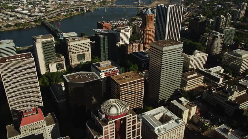 Aerial footage flying over skyscrapers in downtown Portland Oregon capturing the track of KOIN Center and the bustling metropolis in the sunshine