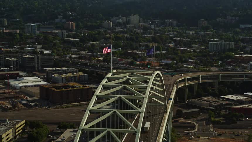 Aerial footage of an American flag flying atop a bridge revealing downtown Portland's skyscrapers and high-rises